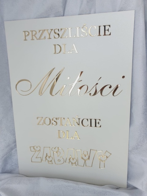 „Biała tablica powitalna z lustrzanym złotym napisem ustawiona na sztaludze.” „Biała tablica powitalna z lustrzanym złotym napisem ustawiona na sztaludze.”